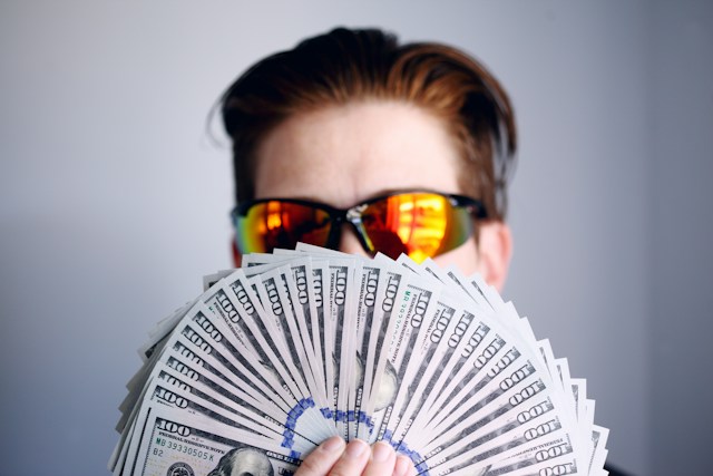 Man wearing sunglasses holding a fan of money in front of his face