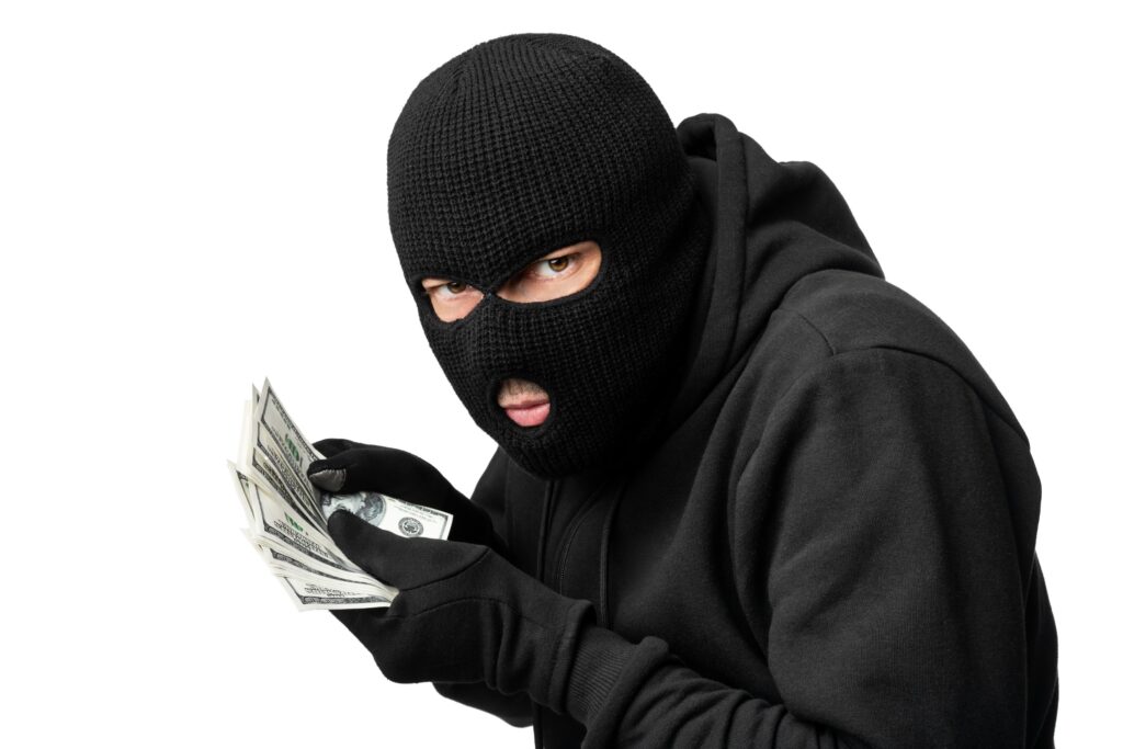 Thief dressed in black with a black mask holding a stack of money